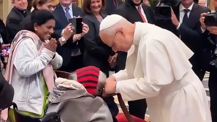 Pope Leo XIV bends down to greet an elderly Indian woman in a wheelchair during a Vatican conference on elder care, symbolizing compassion and dignity for the elderly.